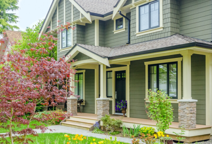 Green craftsman style home with porch with stone columns. Black windows.