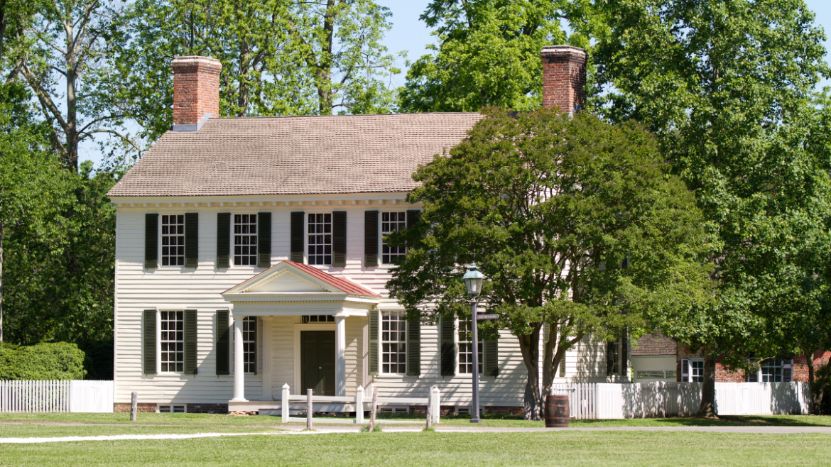 Colonial home with green shutters and hung windows with grids, in white.