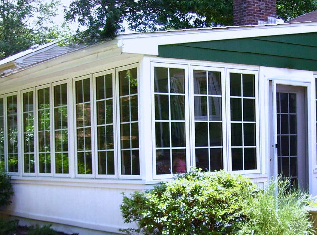 Green home with sunroom addition. Casement windows with grids in white.