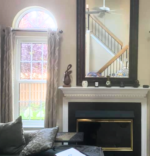 Interior view of double hung windows with architectural, half round windows with grids. Contemporary, black fireplace with large black framed mirror.