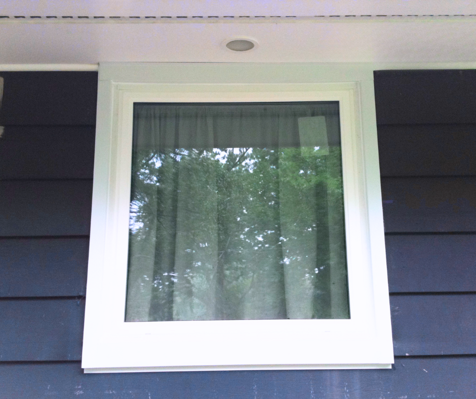 Exterior view of a small, white picture window. Gray, blue siding
